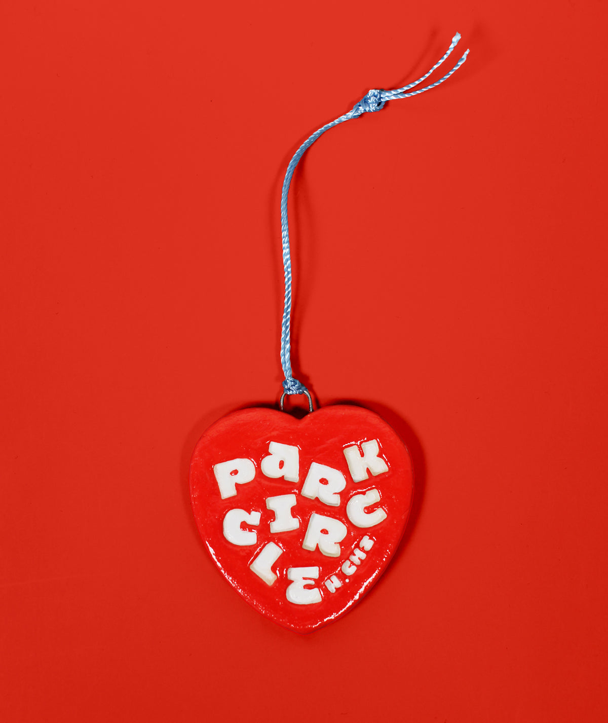 A red heart-shaped hanging ornament with a blue string and white lettering that reads 'PARK CIRCLE' against a solid red background.