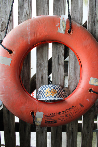 Folly Beach hat. Orange life buoy with a checkered hat inside, hanging on a wooden fence.