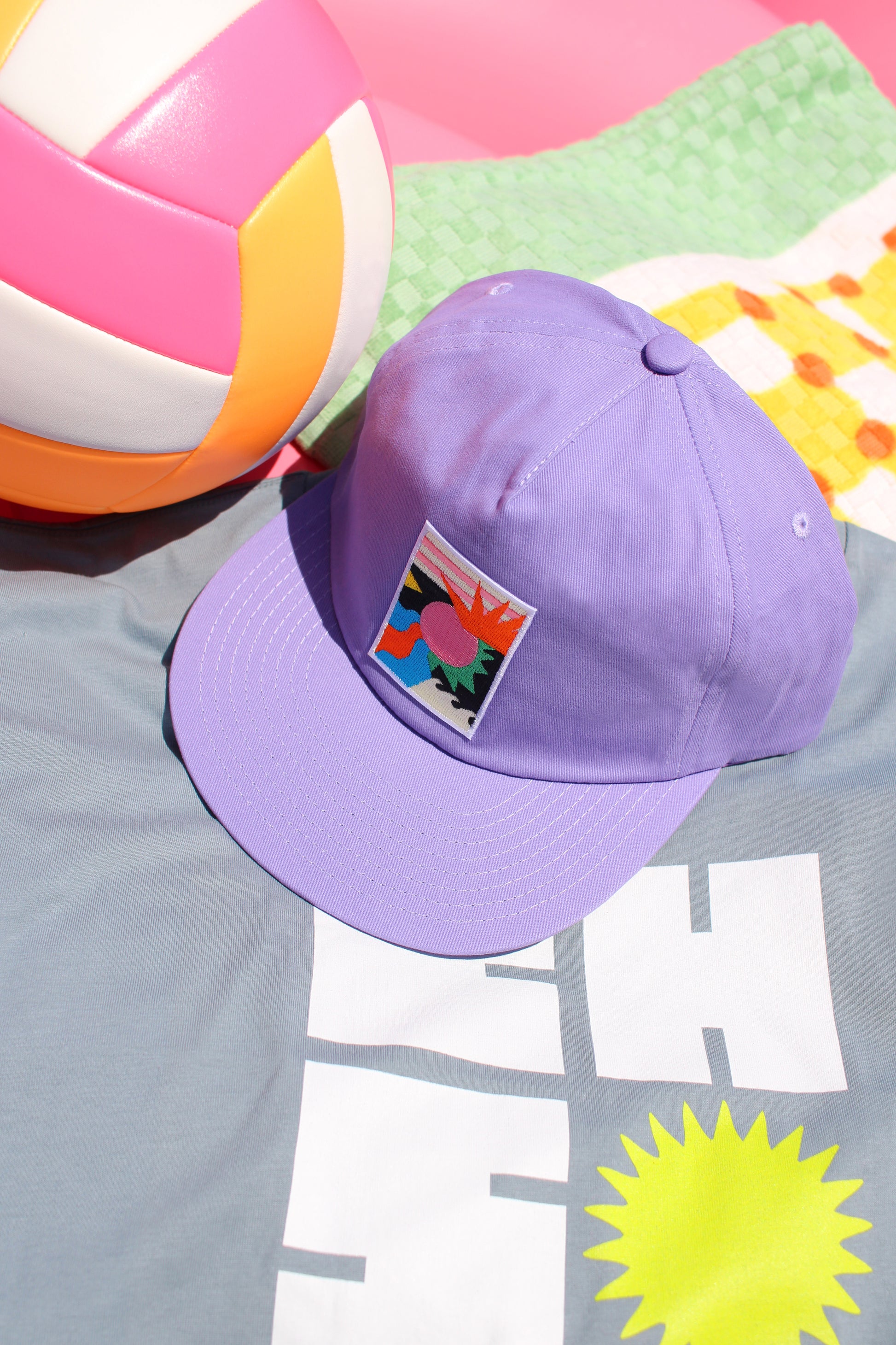 Purple cap with a colorful patch on a surface with a beach ball and towel.