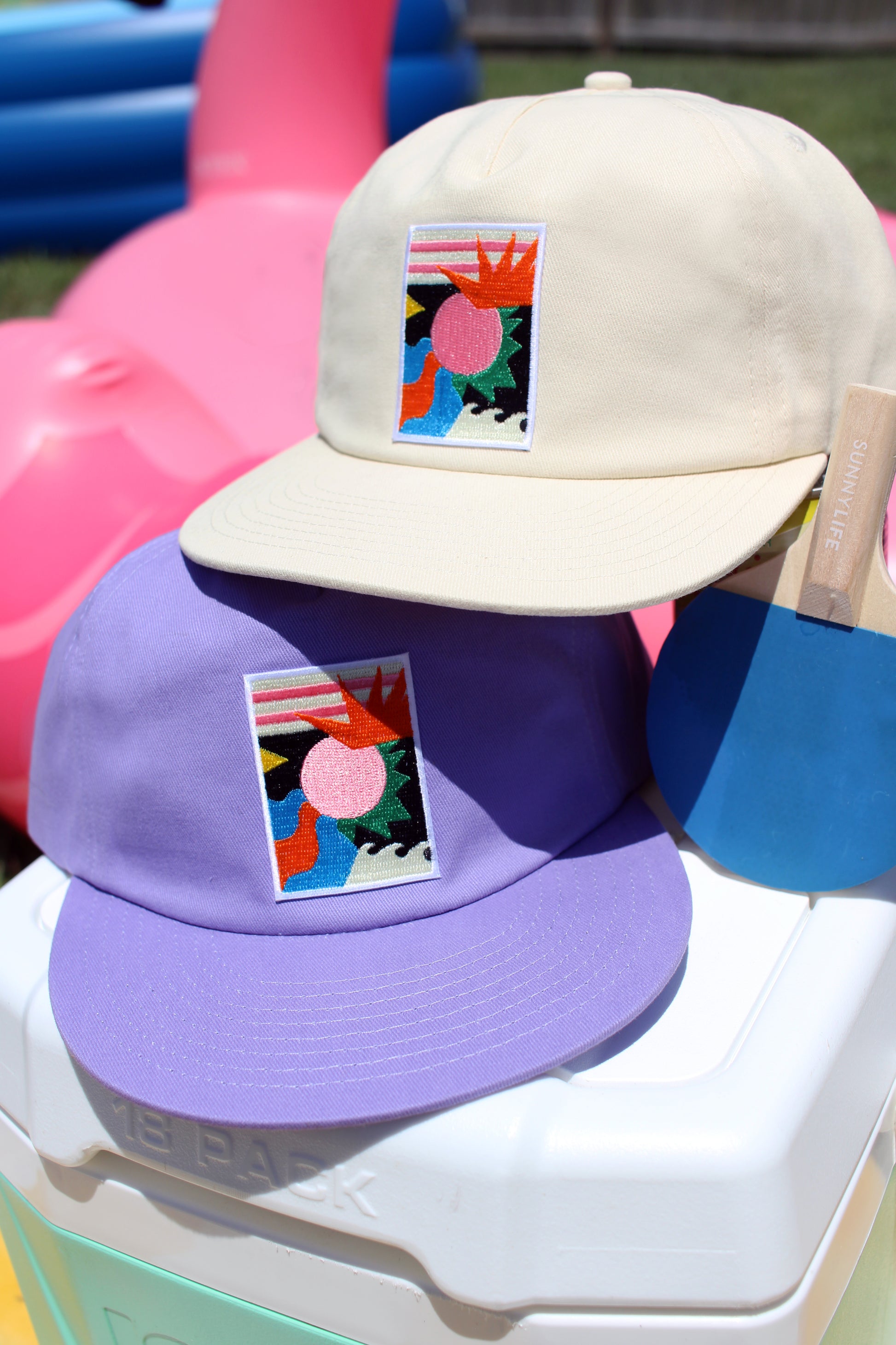 Two hats, one beige and one purple, with colorful designs on a white surface.