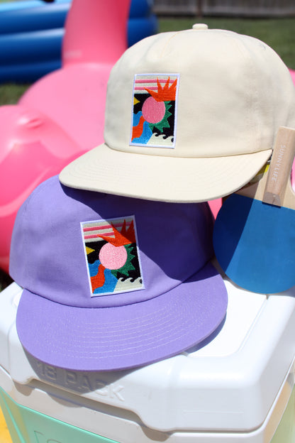 Two hats, one beige and one purple, with colorful designs on a white surface.
