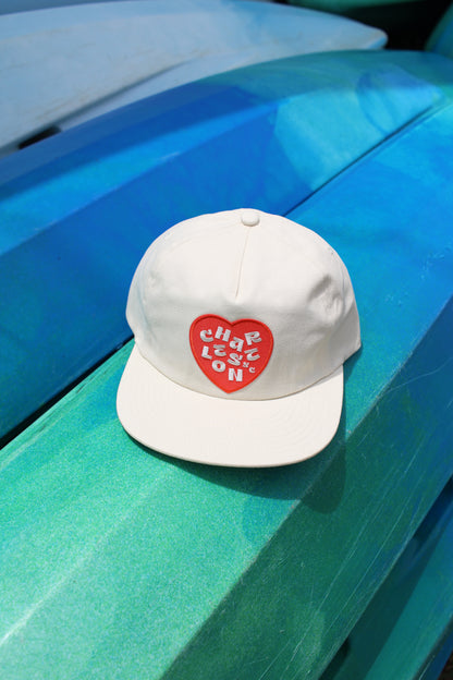 Charleston hat. White cap with a red heart design on a blue surface