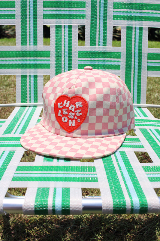 Pink checkered cap with a red heart logo on a green and white striped chair.