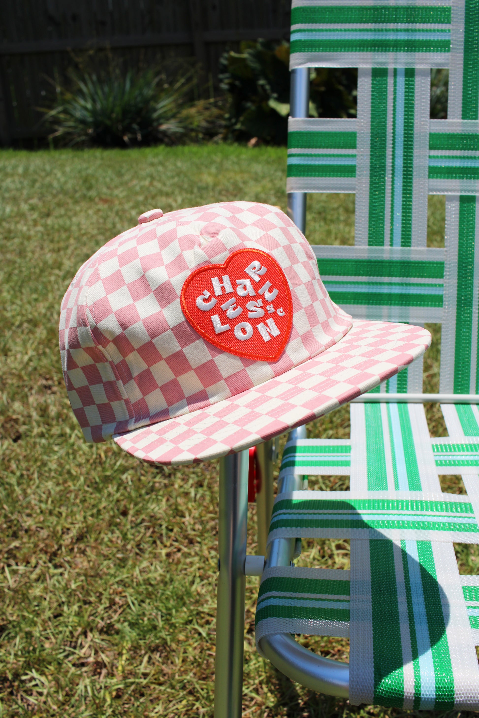 Pink checkered cap with red heart logo on a green lawn chair