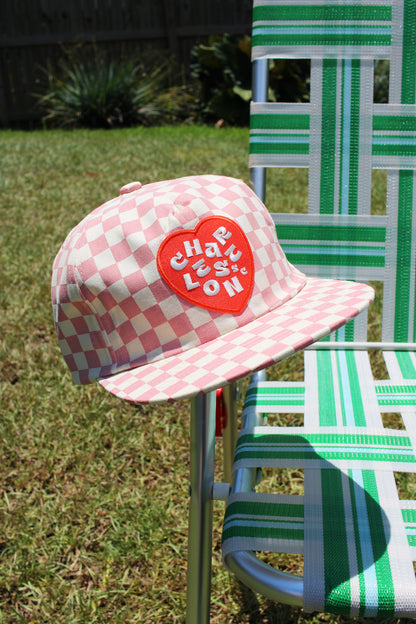 Pink checkered cap with red heart logo on a green lawn chair
