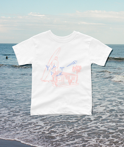 A white short-sleeve t-shirt with a light pink and blue line art graphic of a surfer and beach cabana, displayed against a blurred beach background.