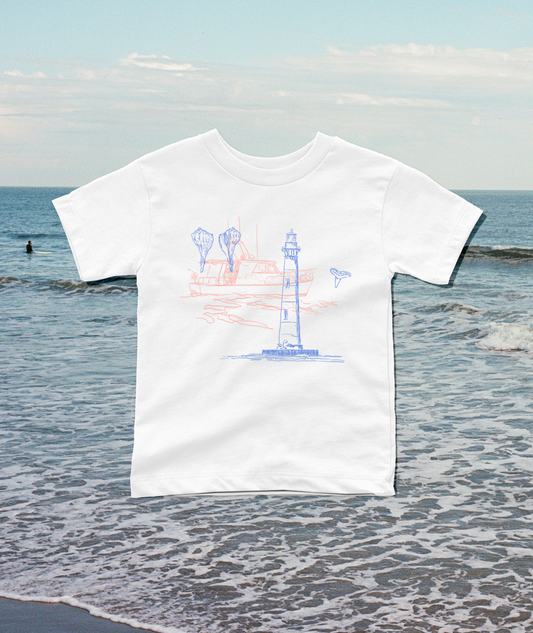 A white short-sleeve crewneck t-shirt with a blue and red line-art graphic of a lighthouse and hot air balloons, shown floating against a beach background with ocean waves and a cloudy sky.