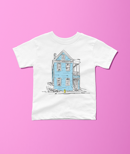 A white short-sleeve crewneck t-shirt featuring a hand-drawn illustration of a light blue house with black sketch lines, displayed flat against a solid pink background.