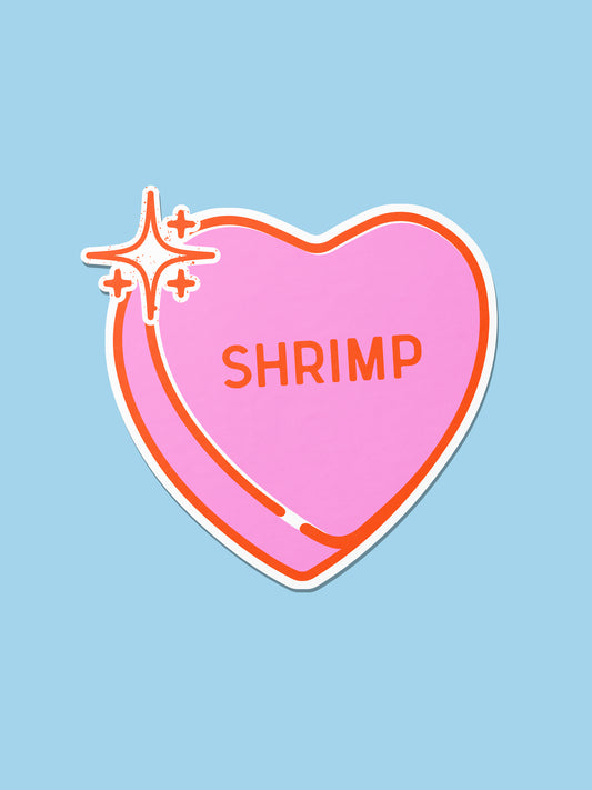 A die-cut sticker shaped like a pink heart candy with orange outlines, white border, and orange text reading 'SHRIMP' on a light blue background.